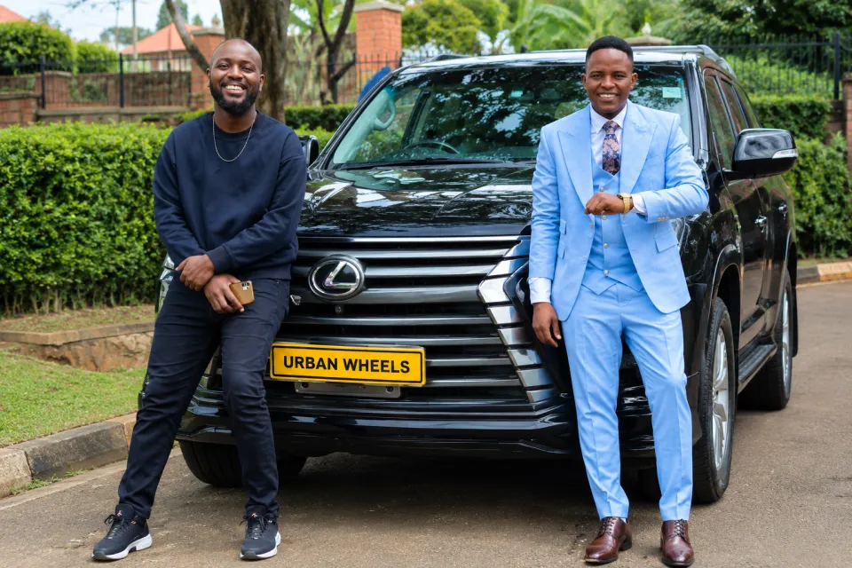 Two smiling clients in front of a black Lexus SUV with an Urban Wheels number plate