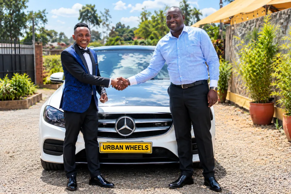 Two men shaking hands in front of a white Mercedes-Benz with an Urban Wheels number plate